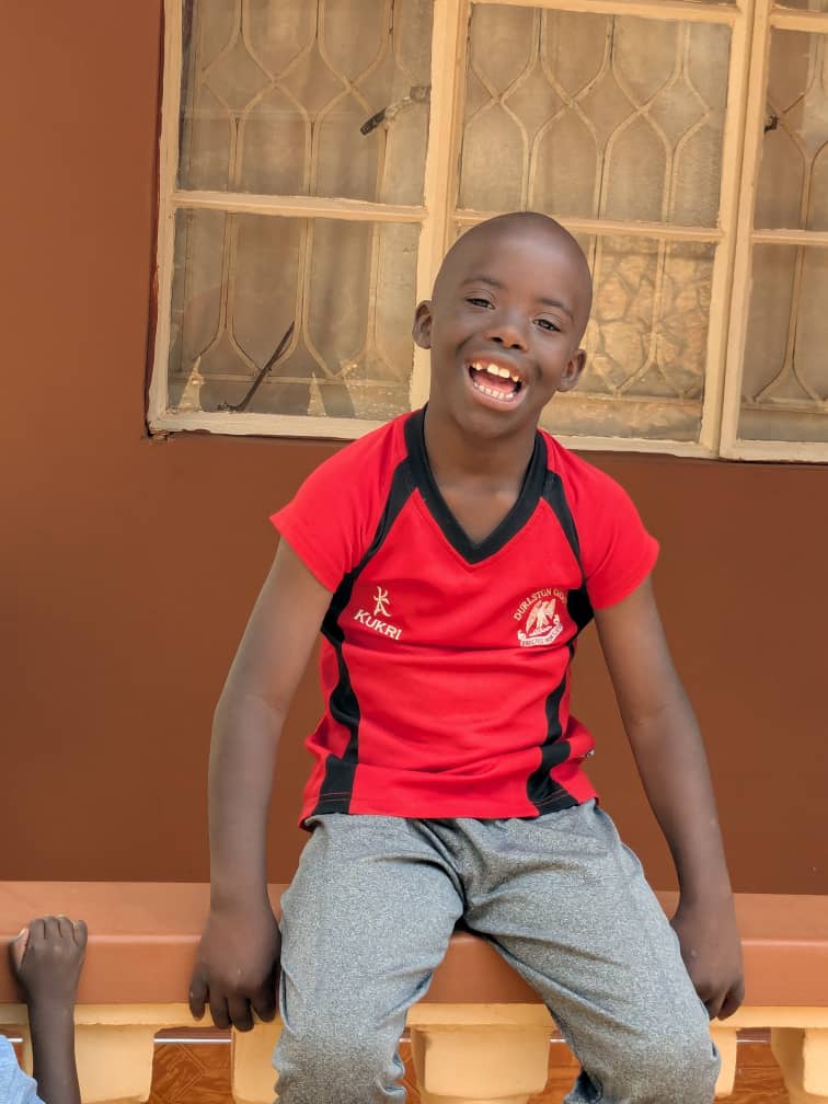 A smiling child in a red shirt seated outside.